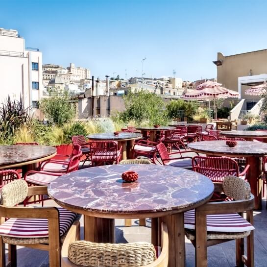 Outdoor seating area with round marble tables and red woven chairs.