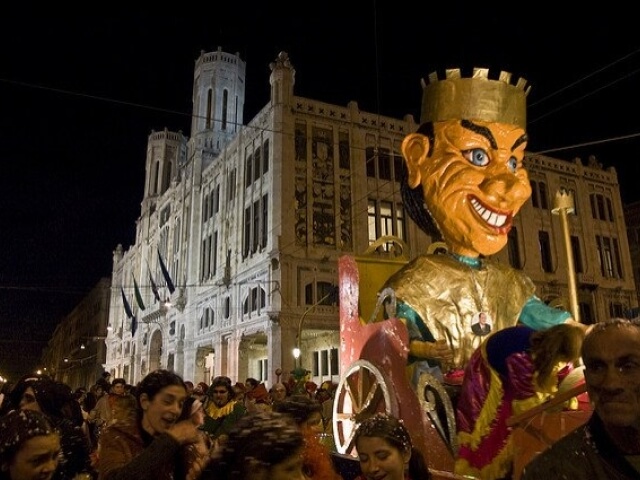 Una folla festosa di persone davanti a un edificio bianco, con un individuo in costume e un'atmosfera notturna vivace.