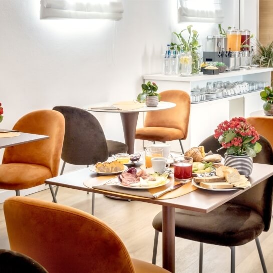 Una luminosa sala da pranzo moderna con tavoli imbanditi di cibo e piante, creando un'atmosfera accogliente.