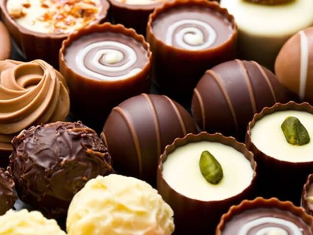 Collezione di cioccolatini di diverse forme e dimensioni, con guarnizioni di pistacchi e nocciole, disposti casualmente.