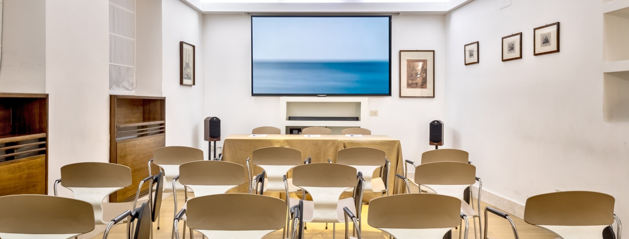 Sala di presentazione con sedie, tavolo, schermo e decorazioni.