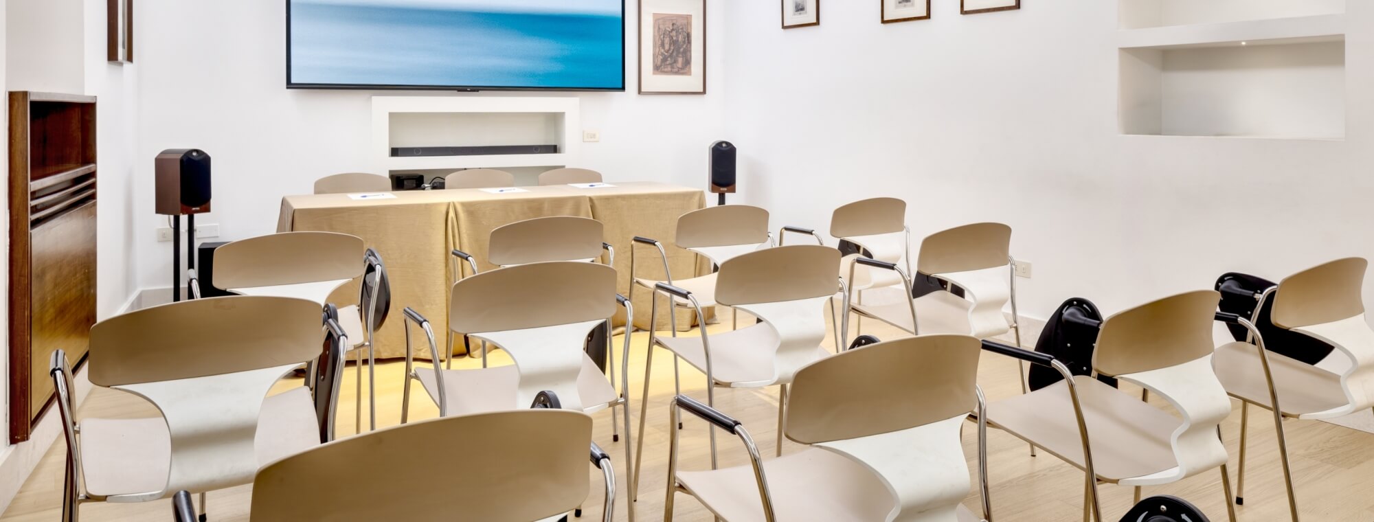 Sala riunioni con sedie, tavolo dorato e schermo grande.
