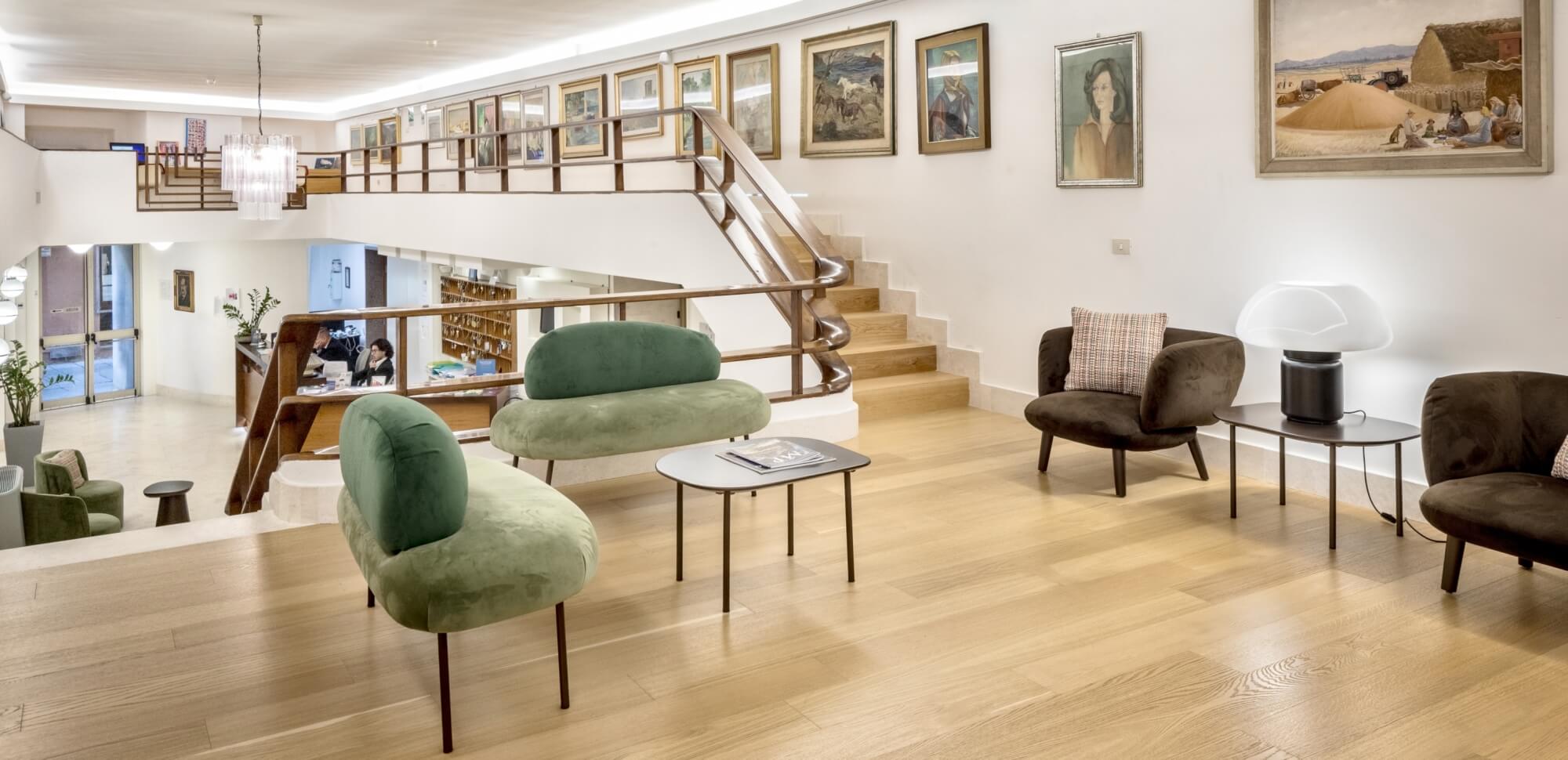 Lobby di hotel con divani, reception e scala in legno.