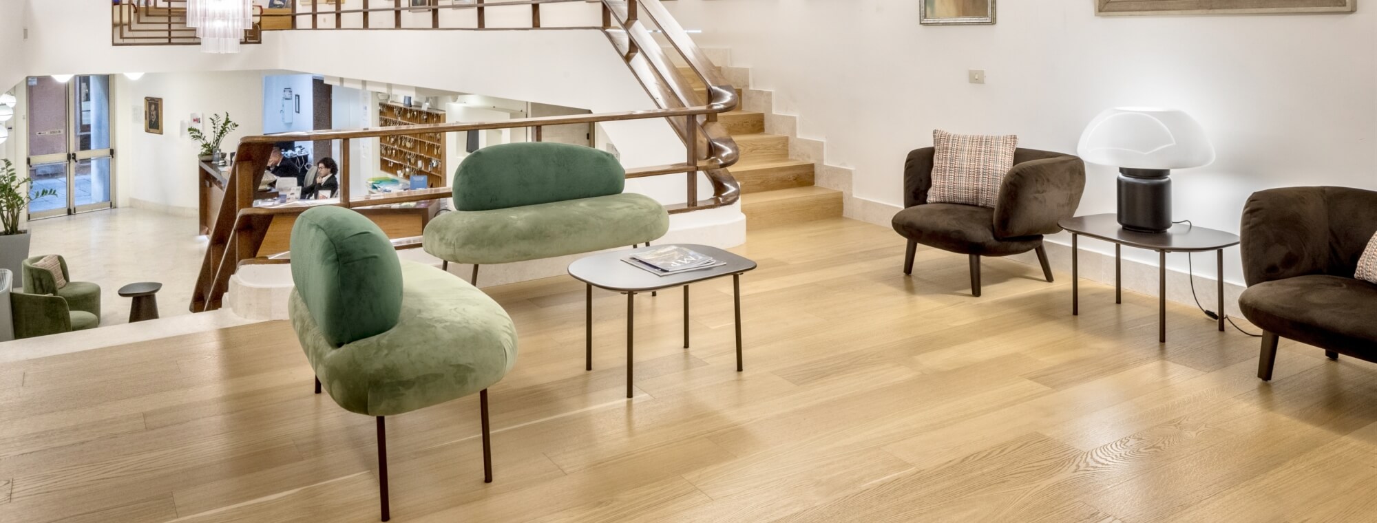 Hotel lobby with green velvet seating, wooden floor, and reception desk.