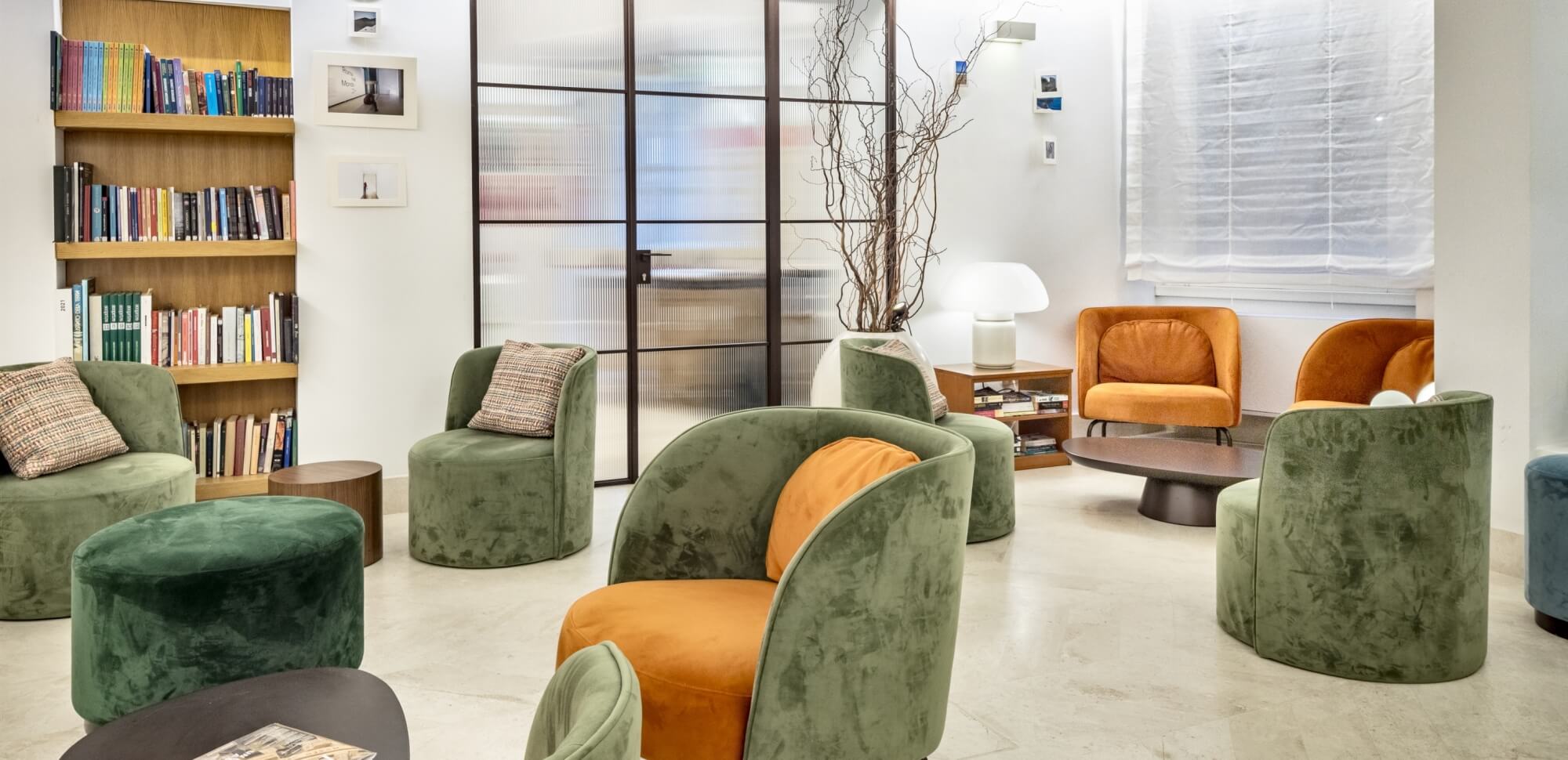 Area lounge con poltrone in velluto, librerie e lampada a fungo.