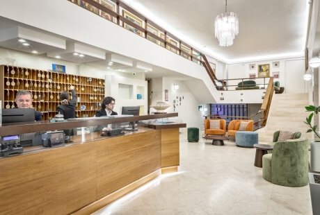 Area reception di hotel con personale, cubby, scale e poltrone.