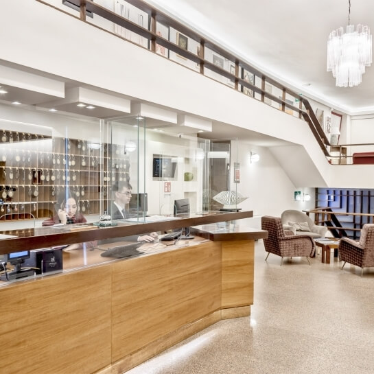 Lobby moderna con reception in legno chiaro, chandelier, sedie eleganti e decorazioni, suggerendo lusso e comfort.