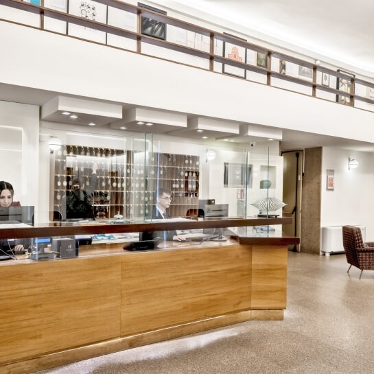 Spazio ufficio aperto su due livelli con scrivania frontale, barriere di vetro e un'area reception.