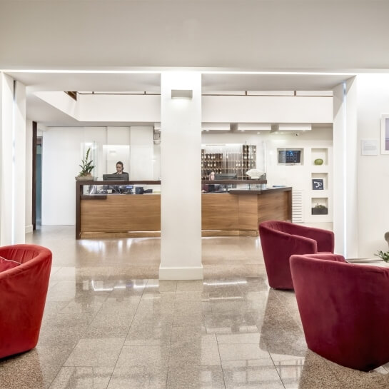 Lobby moderna e minimalista con sedie rosse, pavimento lucido, controsoffitto bianco e opere d'arte eleganti.