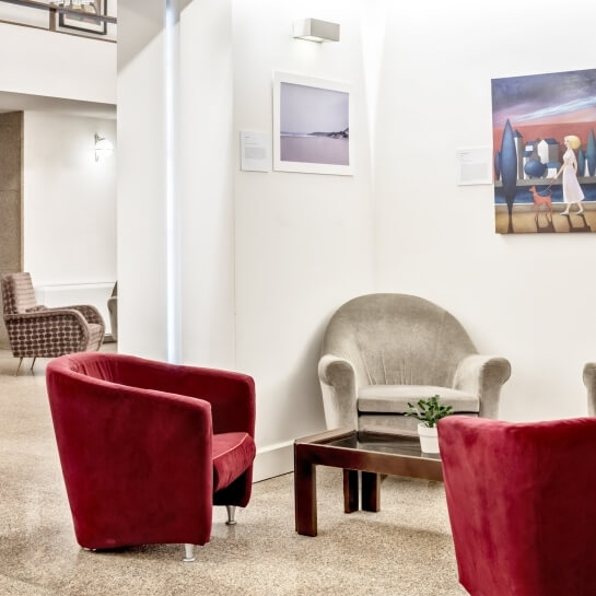 Soggiorno moderno minimalista con pareti bianche, opere d'arte, sedie rosse e un tavolo con pianta, atmosfera serena.