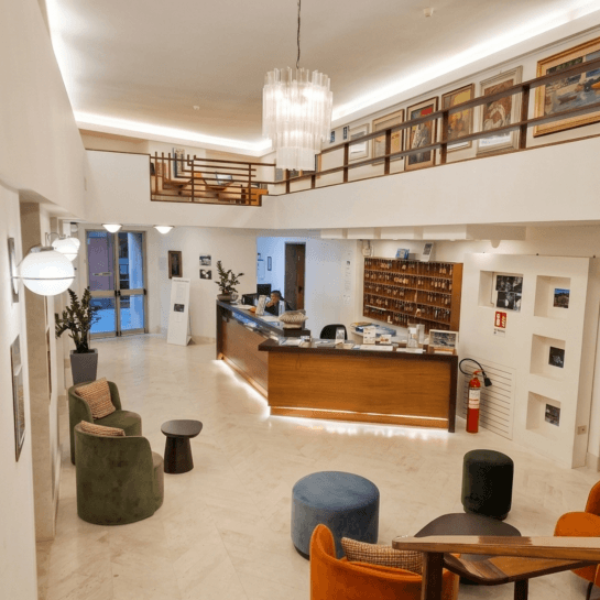 Hotel reception area with wooden desk, seating, chandelier, and artwork.