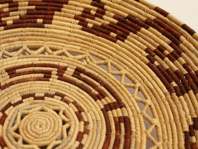 Primo piano di un cesto intrecciato con un design a spirale in rattan, con strisce di colore tan e marrone scuro.