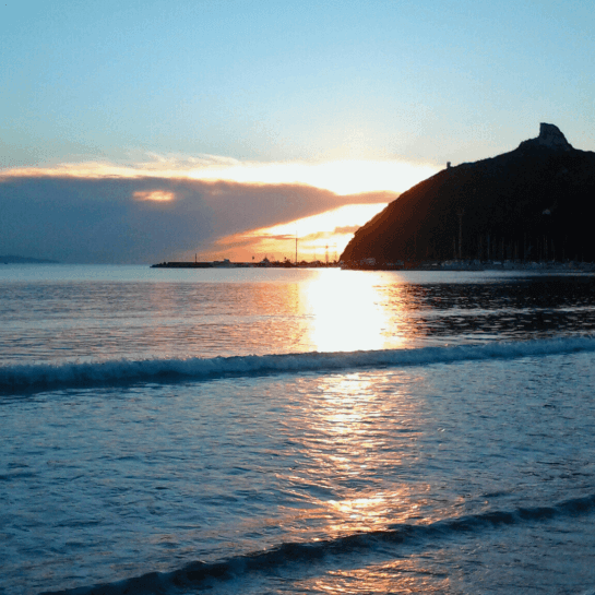 Una scena serena dell'oceano al tramonto, con montagne sullo sfondo e riflessi dorati sull'acqua calma.