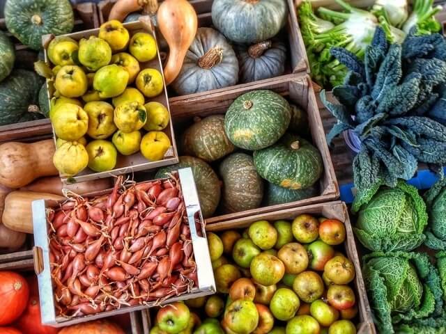 Un assortimento vibrante di frutta e verdura fresche in casse di legno, con mele, squash e cipolle rosse.