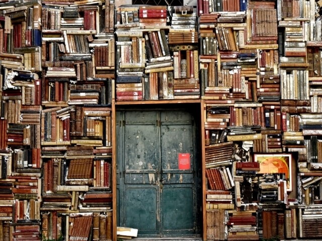 Una porta verde scuro circondata da una collezione di libri di varie dimensioni e colori.
