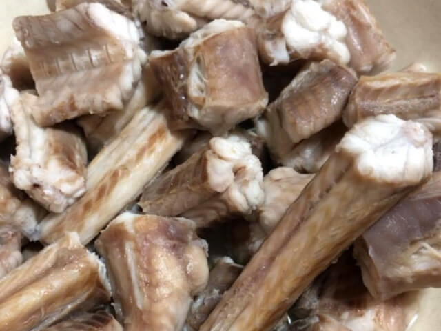 Un primo piano di un mucchio di costine cotte, con carne tagliata a pezzi e ossa visibili, su uno sfondo beige.