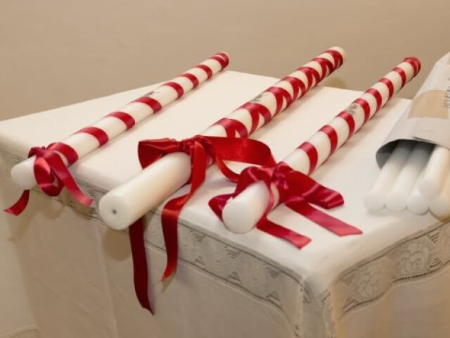 Tre candele bianche con strisce rosse e nastri rossi su una tovaglia bianca, pronte per un evento festivo.