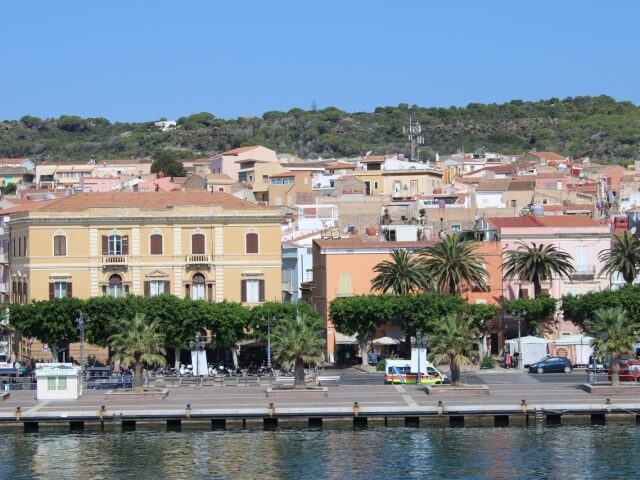 Una tranquilla città costiera con un grande edificio giallo, alberi, un molo e acqua blu serena sullo sfondo.