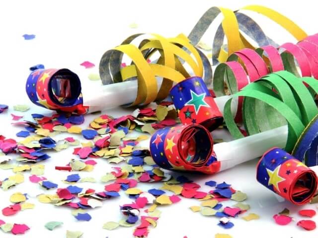 Scena festiva con favori di carta colorati e coriandoli a forma di cuore su una superficie bianca.