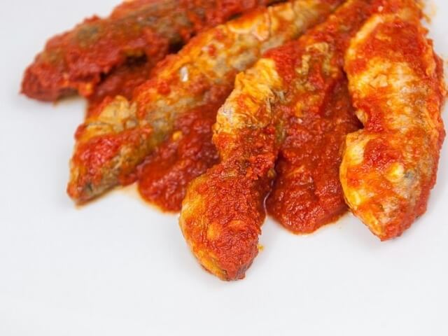 Pesce in salsa rossa su superficie bianca, con tonalità marrone chiaro e bordi più scuri, creando un piatto appetitoso.