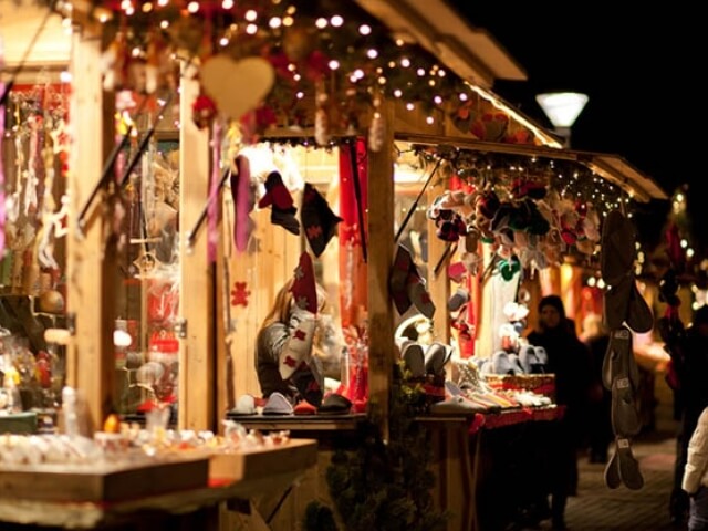 Mercatino di Natale festivo con un banco di legno decorato, luci, e una varietà di articoli in vendita. Atmosfera gioiosa.