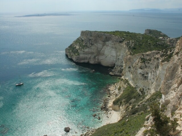 Scogliera rocciosa con vegetazione, spiaggia sabbiosa, oceano turchese e cielo blu, creano un'atmosfera serena.