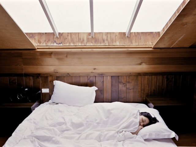 Una donna dorme serenamente in un letto, circondata da un'accogliente stanza con pareti in legno e una finestra sul tetto.