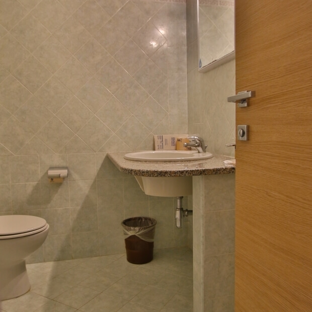 Immagine di un bagno pulito con toilet bianco, lavabo con piano in granito, specchio e porta a destra.