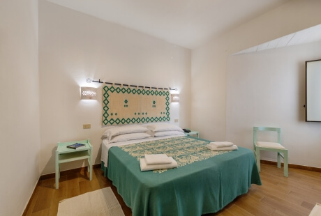 Camera da letto serena con letto centrale, comforter teal, pareti verdi, illuminazione soffusa e decorazioni geometriche.