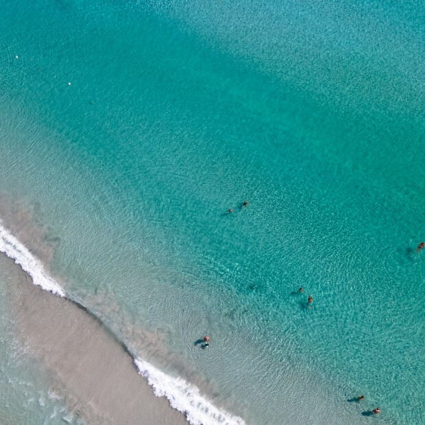 Una vista aerea di una spiaggia serena con oceano turchese, onde gentili e persone che si godono il sole e l'acqua.