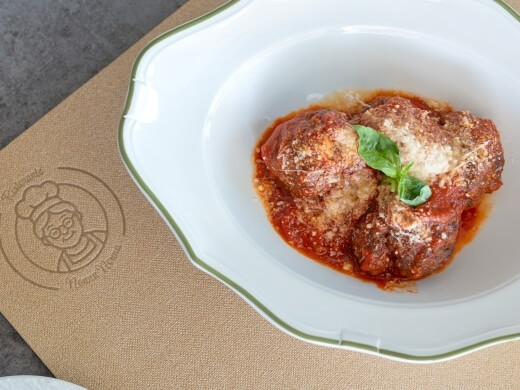 Pollo in salsa rossa con formaggio e basilico su piatto bianco.