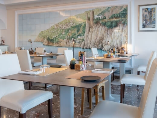 Tavoli da pranzo con impostazioni in una stanza con murale costiero.