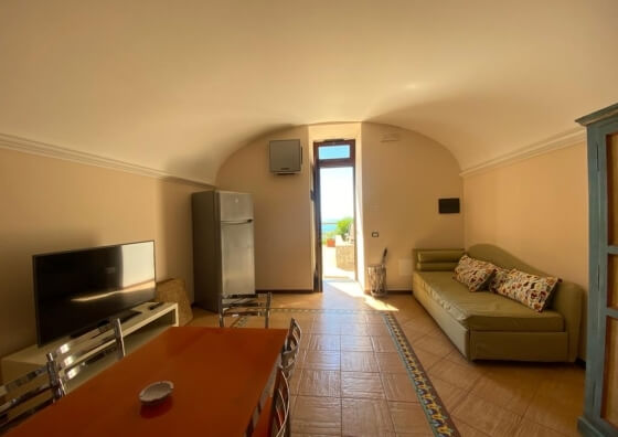 Soggiorno con TV, tavolo da pranzo, divano e vista mare.