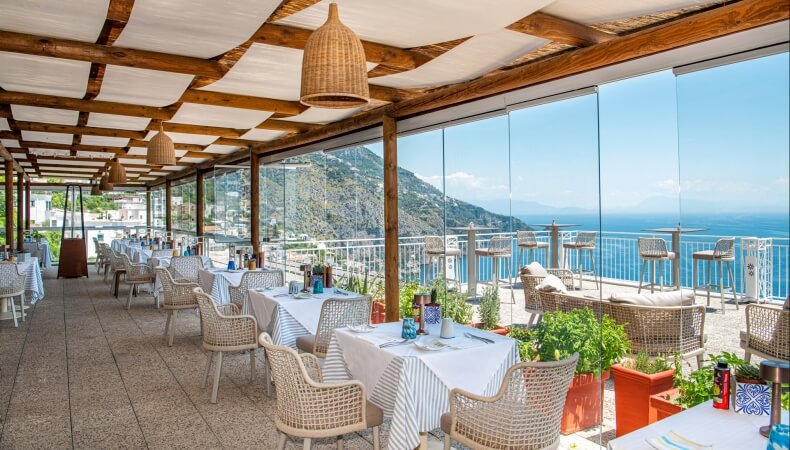 Area pranzo all'aperto con vista oceano, tavoli decorati e riscaldatori.