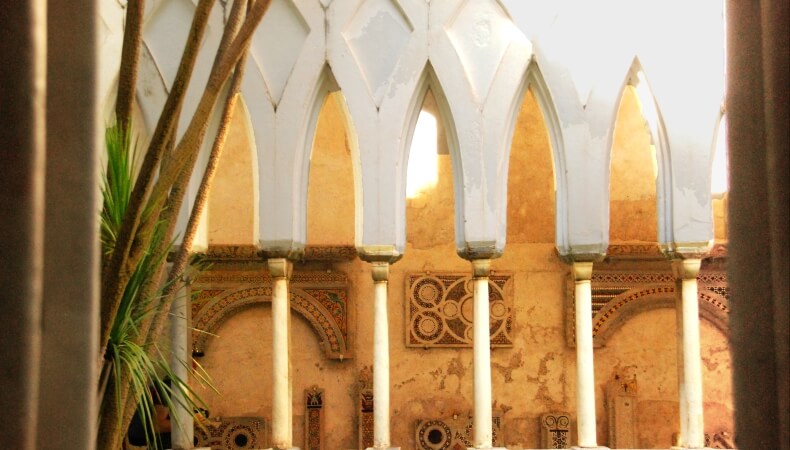 Struttura con colonne bianche, soffitto decorato e palma a sinistra.