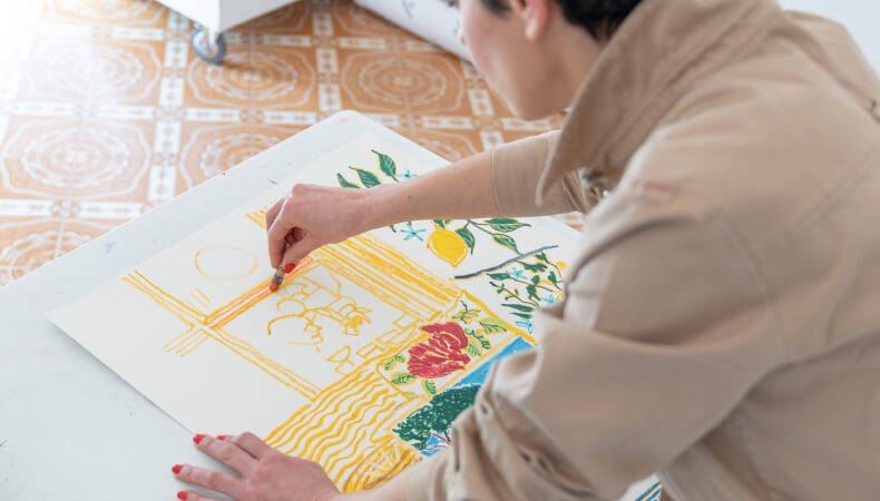 Person in tan jacket drawing with crayons on large paper.