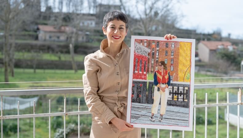 Woman in tan jumpsuit holds drawing of another woman with buildings.
