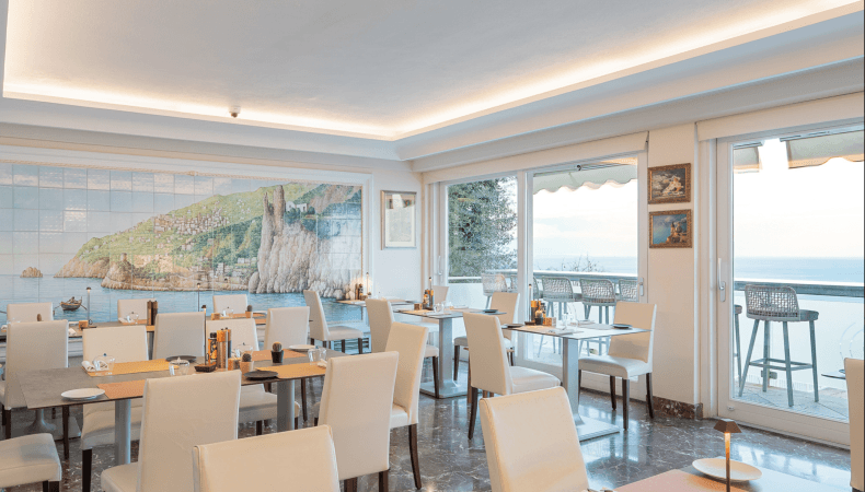 Dining area with white chairs, coastal mural, and ocean view.