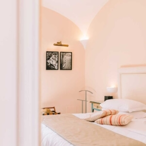 Cozy pink bedroom with a bed, pillows, lamp, and framed pictures.