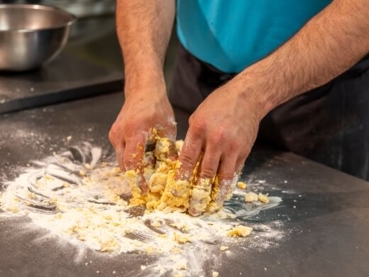Mani lavorano l'impasto giallo e bianco su una superficie scura.