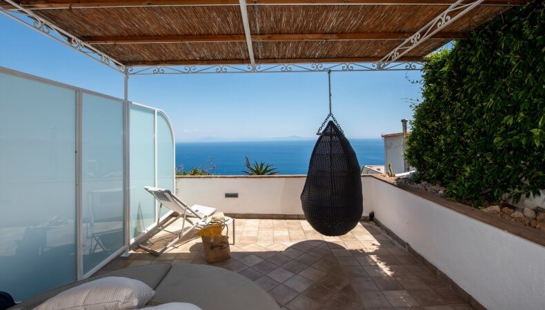 Terrazza con vista mare, poltrona a sospensione e sedie a sdraio.