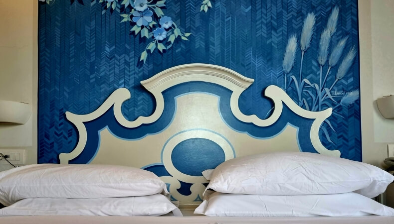 Camera d'hotel con letto, testiera decorativa e carta da parati blu.