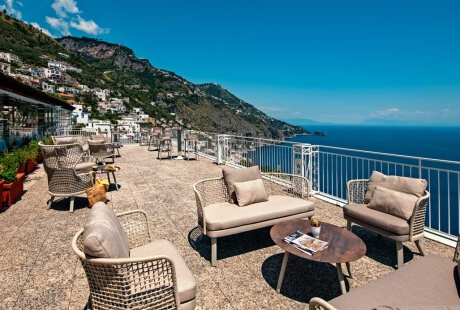 Outdoor seating area with woven furniture, ocean view, and clear sky.