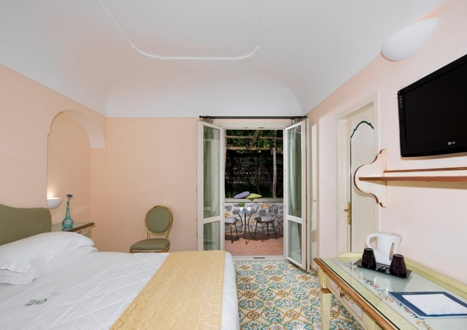Camera d'hotel con letto, sedia verde e porte francesi.