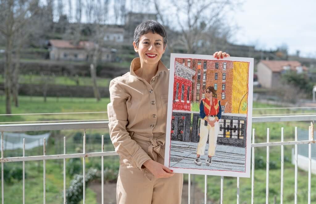 Woman in tan jumpsuit holds a city street drawing.