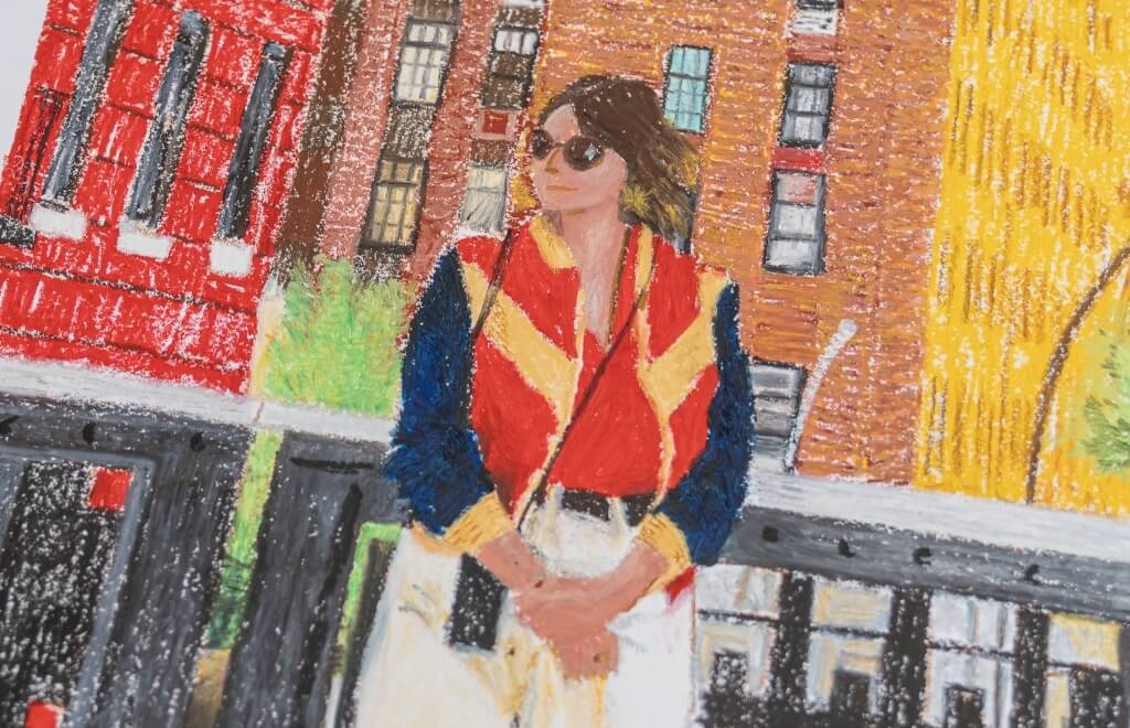 Person in striped jacket and sunglasses stands before brick buildings.