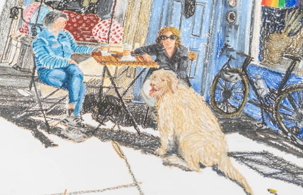 Two people at an outdoor cafe with a dog and a rainbow flag.