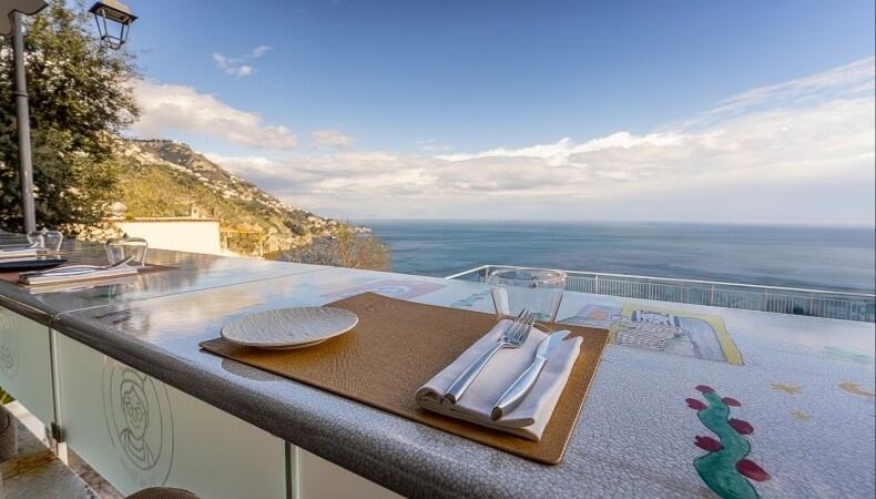 Tavolo da pranzo con vista mare, piatti e bicchiere d'acqua.