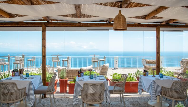 Area ristorante all'aperto con vista sull'oceano e tavoli decorati.