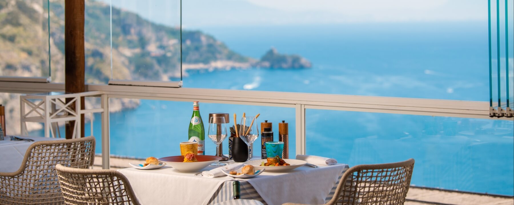 Tavolo imbandito con cibo e vista su acqua e montagne.